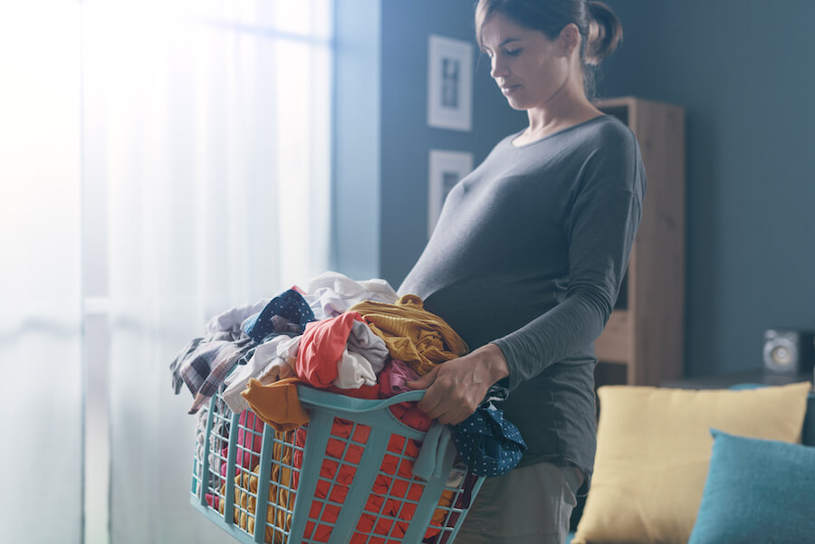 A photo of a pregnant woman carrying a big load of laundry overflowing from a plastic laundry basket.