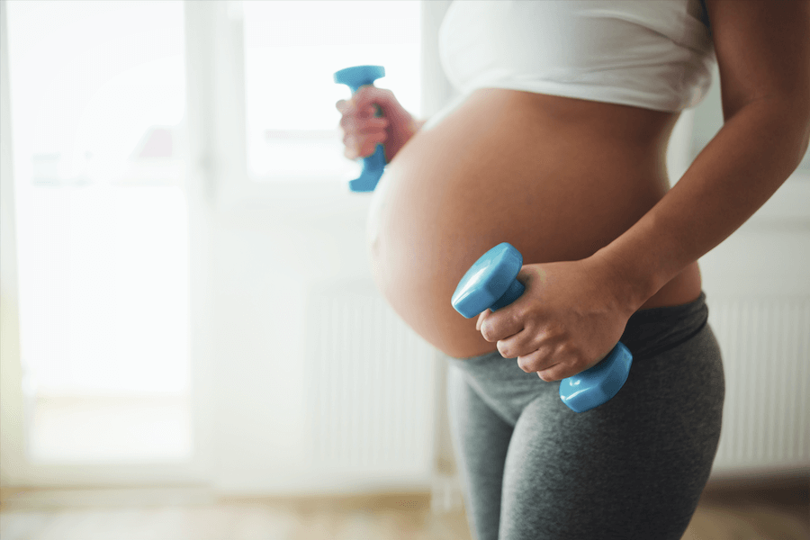 A photo of a pregnant woman getting some exercise while holding 2 dumbbells. 