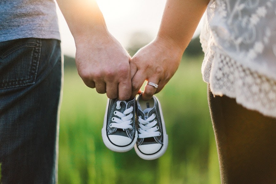 A husband and wife are holding hands with a pair of baby shoes in between them 