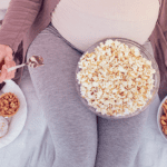 pregnant woman sitting with popcorn and other pregnancy cravings