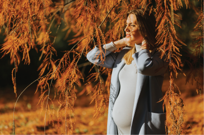 Fall maternity photo of a pregnant woman looking into the distance while standing under a fall colored tree.