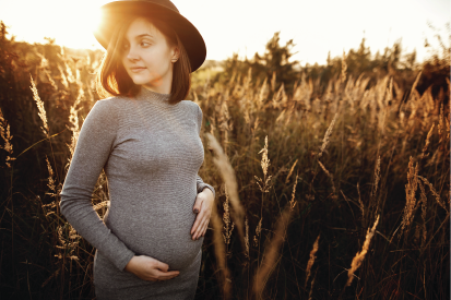 Pregnant woman standing in field during golden hour holding her bump.