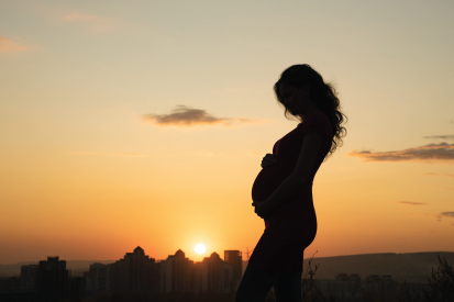 Silhouette of a pregnant woman with a sunset over the city skyline in the background.